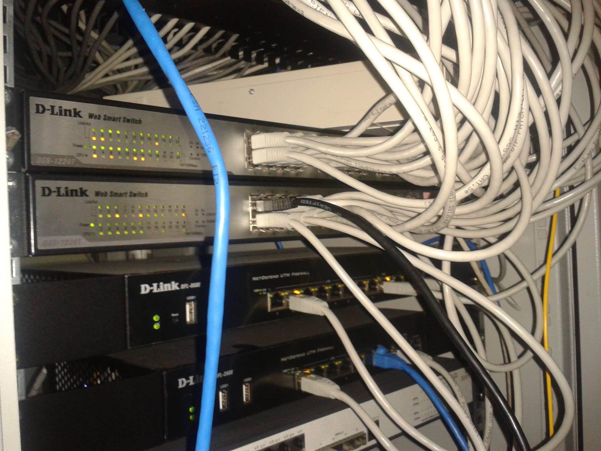 Network switches and firewalls stacked in a rack inside a server room, with bundles of cables.