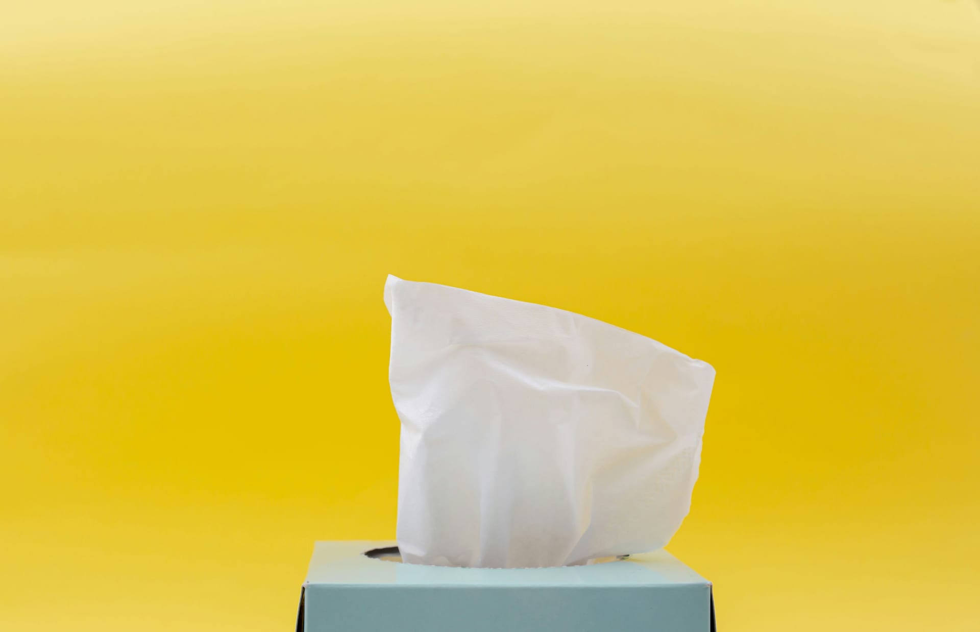 Vista superior de pañuelos de papel blancos y arrugados saliendo de una caja de cartón azul sobre una superficie clara.