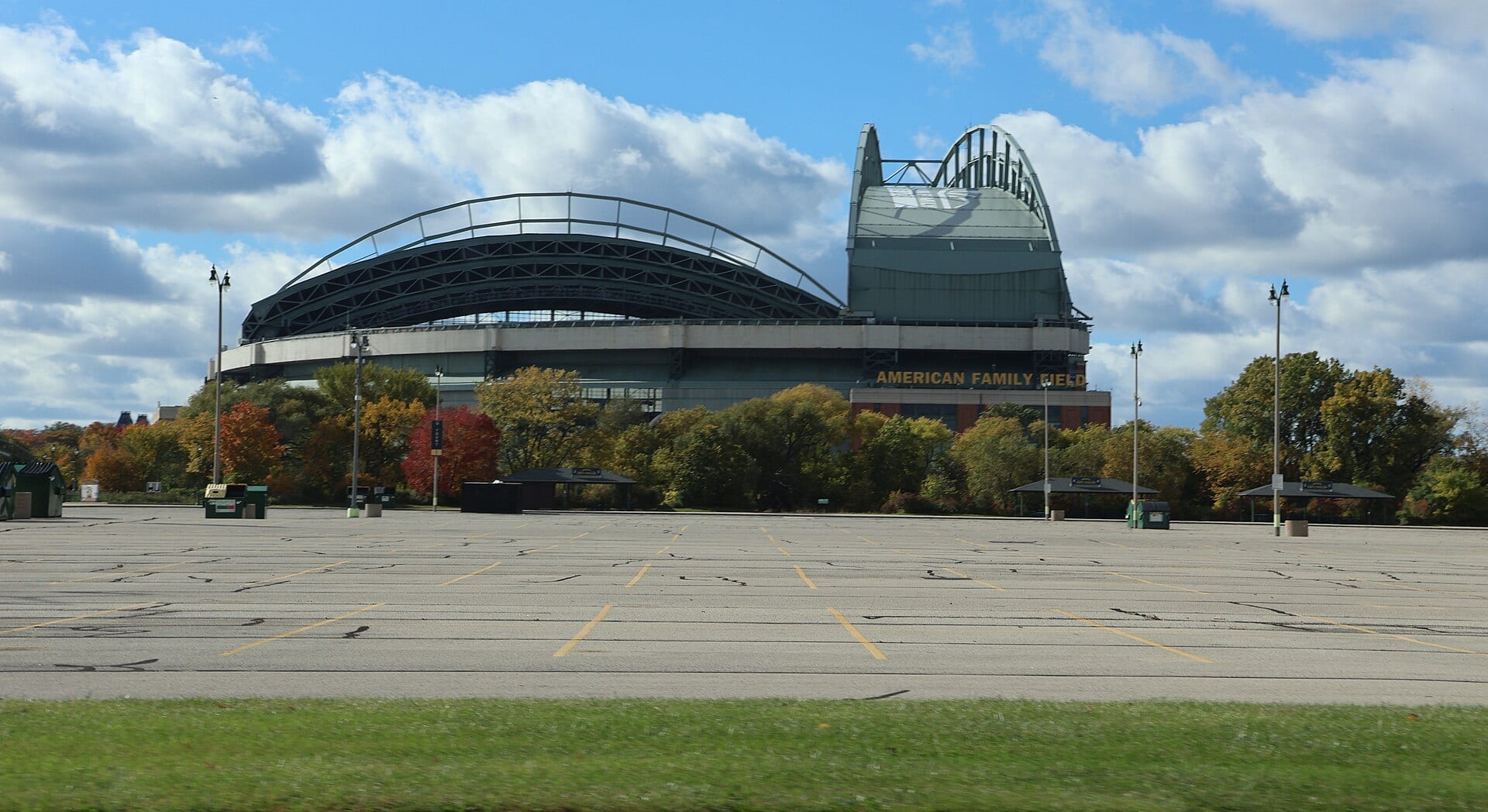 The exterior of American Family Field in Milwaukee behind an empty parking lot and trees in autumn colors.