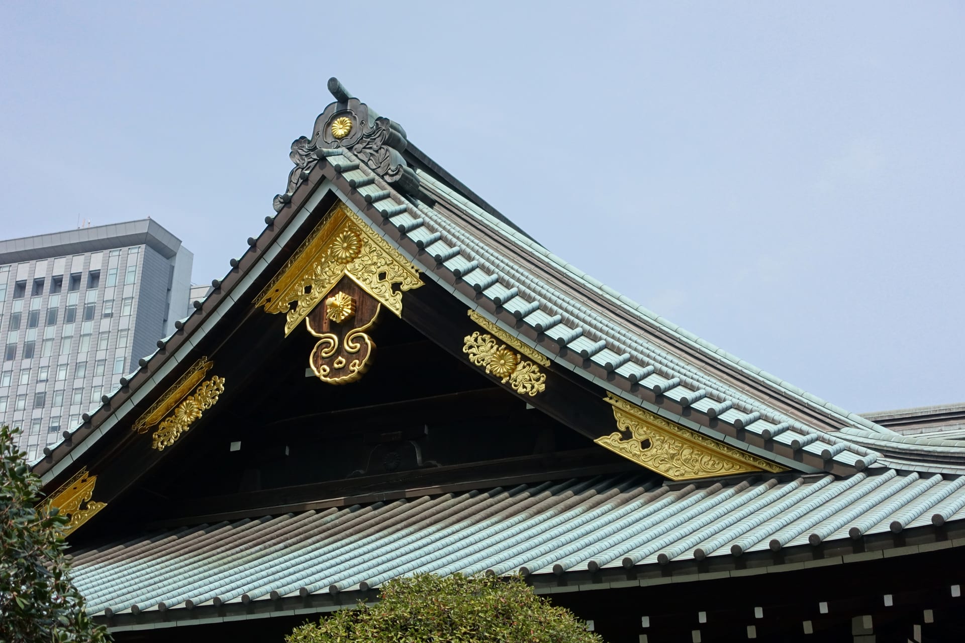The eave of a green-tiled roof with gold chrysanthemum-shaped ornaments, and a glass office tower behind it under a clear sky. File photo.
