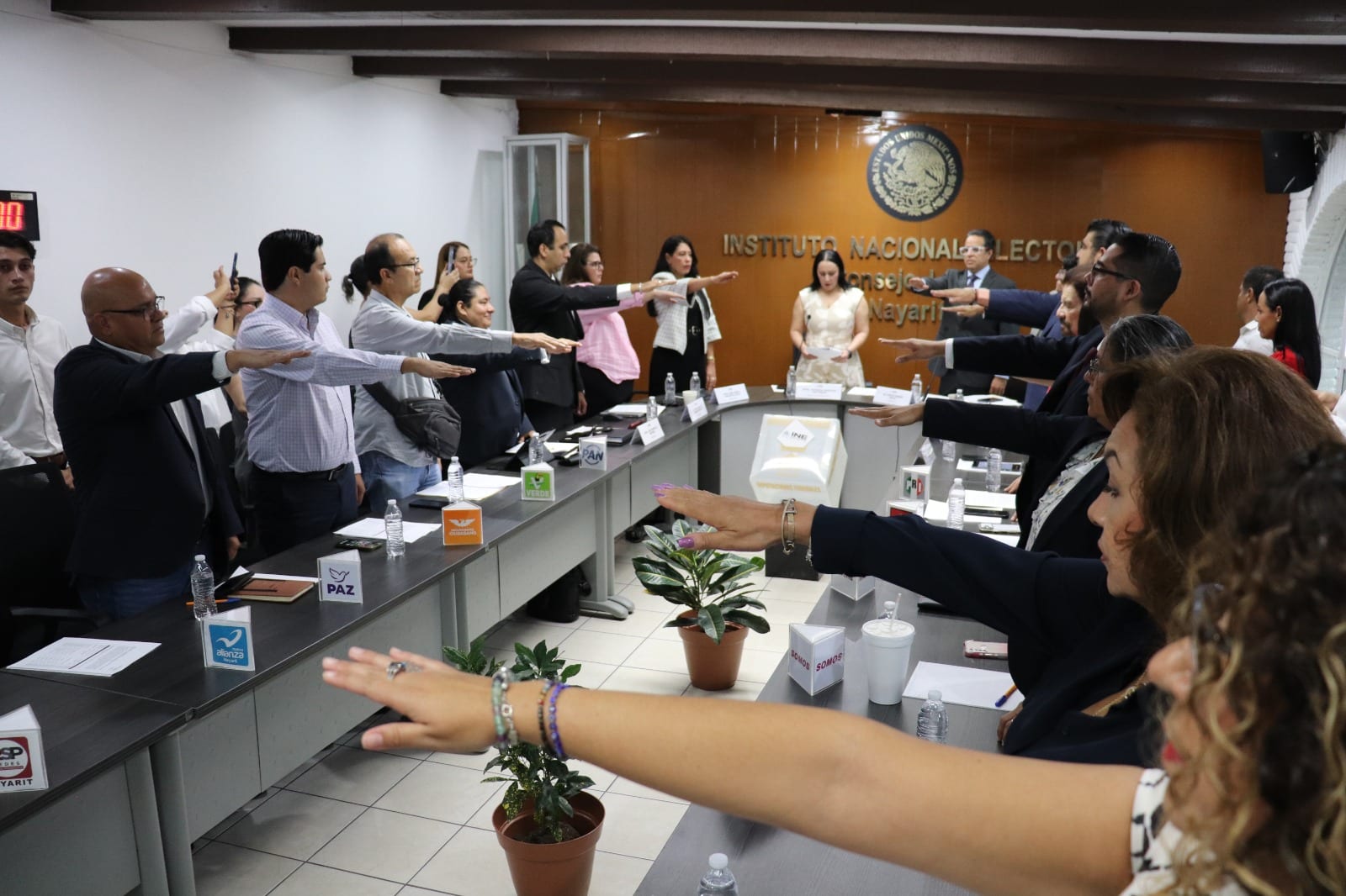 Integrantes de un consejo local del INE levantan la mano derecha para rendir protesta en una sala con el escudo nacional al fondo.