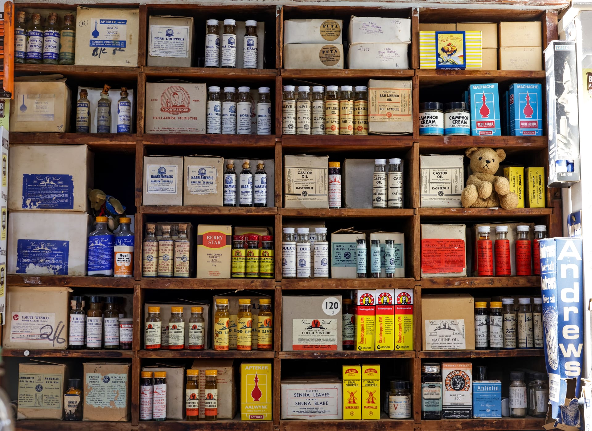 Estante de madera de una botica antigua con frascos de vidrio y cajas de medicamentos ordenados en repisas.