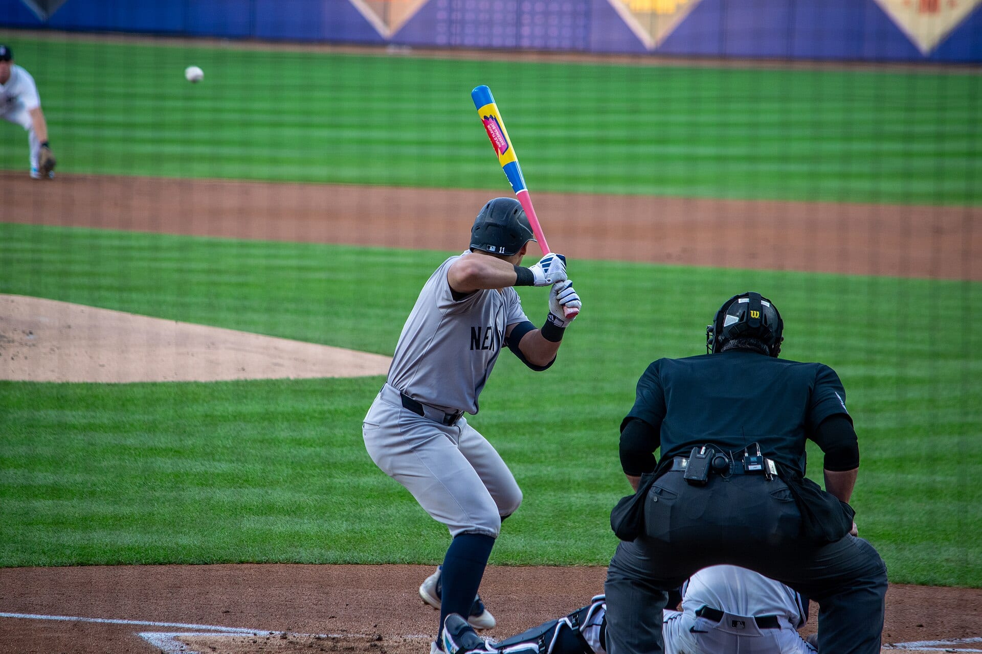 Un bateador de los Yankees, con casco y camiseta gris, espera un lanzamiento mientras el umpire se agacha detrás de él.