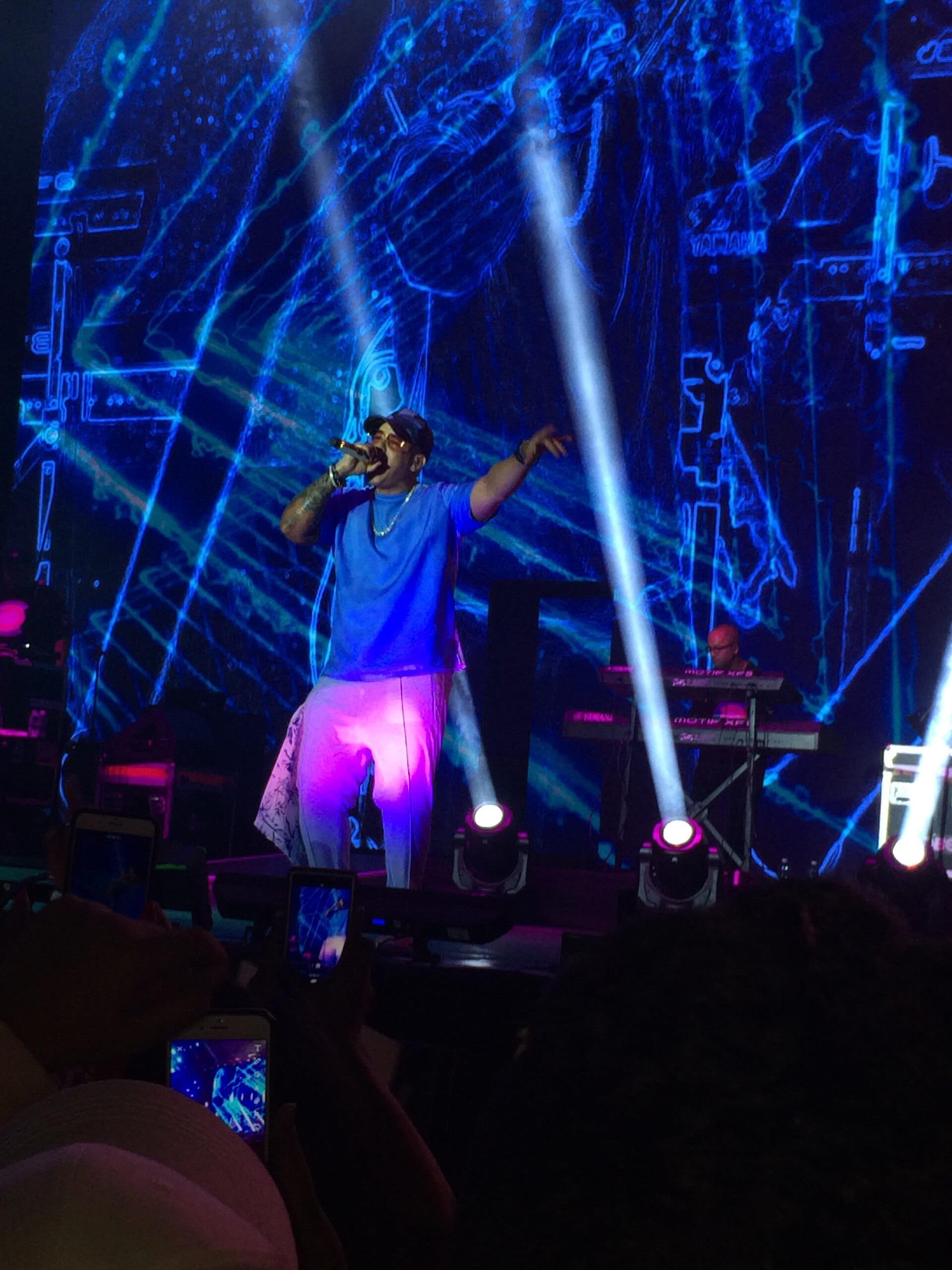 Daddy Yankee canta con el micrófono en la mano y un brazo extendido sobre un escenario de luces azules y moradas.