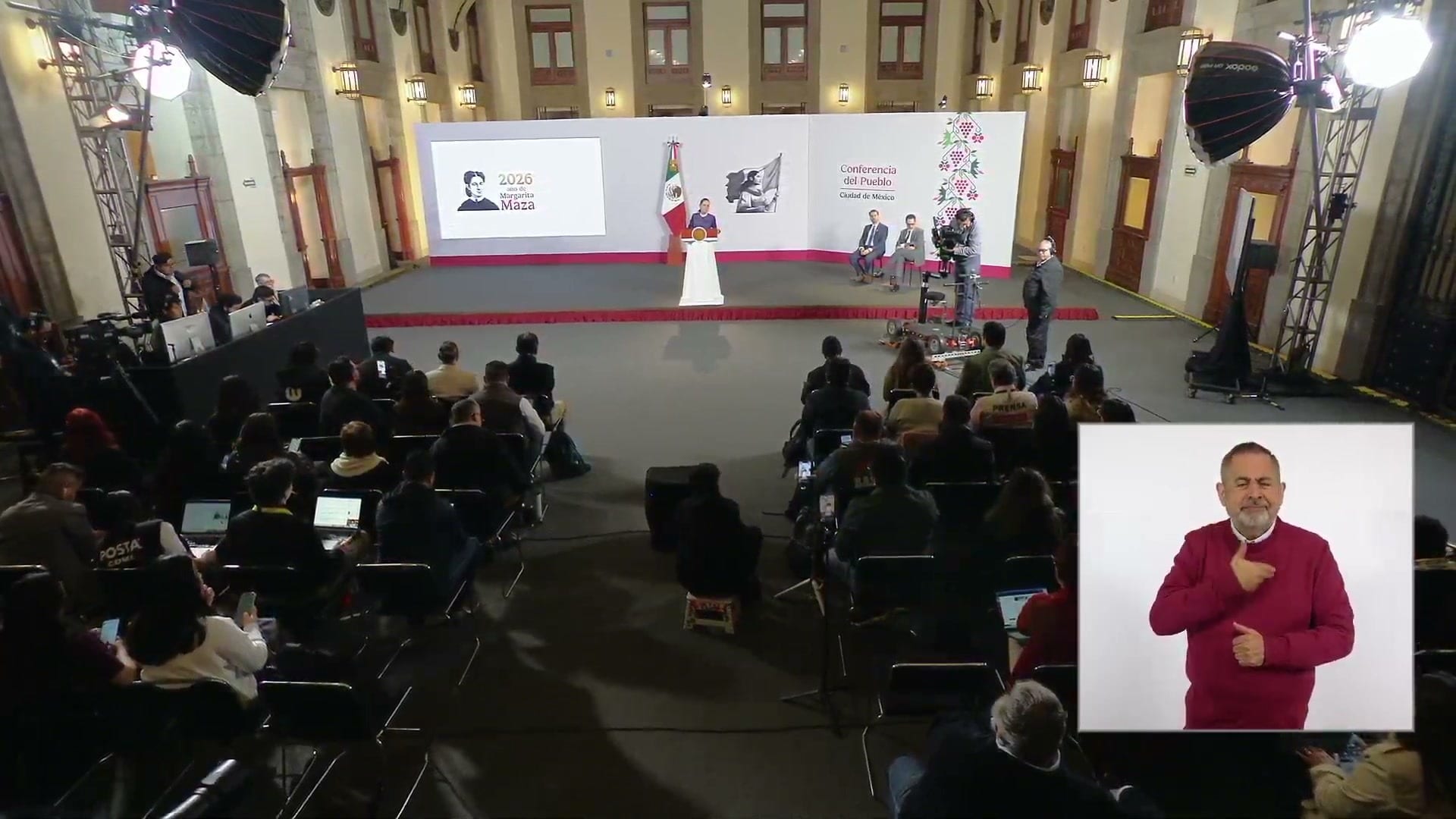 La presidenta habla desde el podio en el salón de la conferencia matutina, con reporteros sentados al frente y un intérprete de lengua de señas en un recuadro.