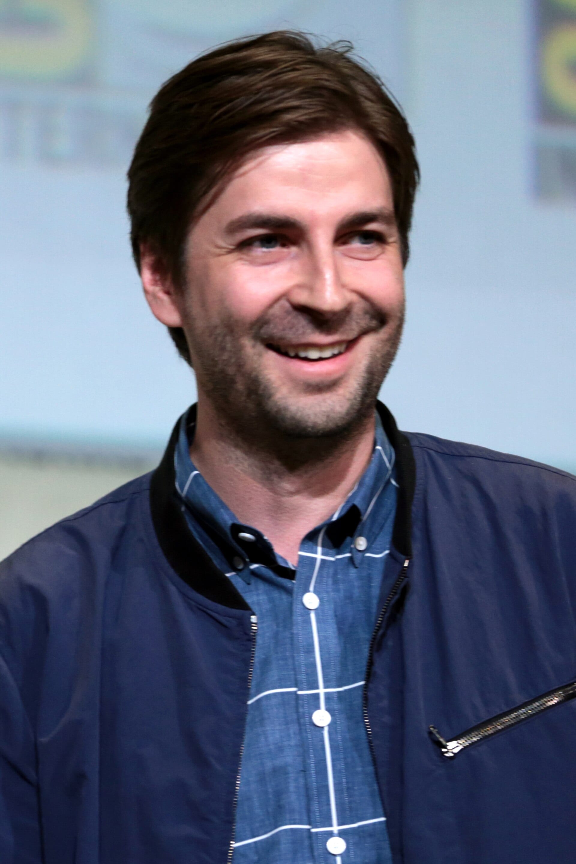 Jon Watts, con barba y camisa oscura, habla frente a un micrófono en un panel de convención.