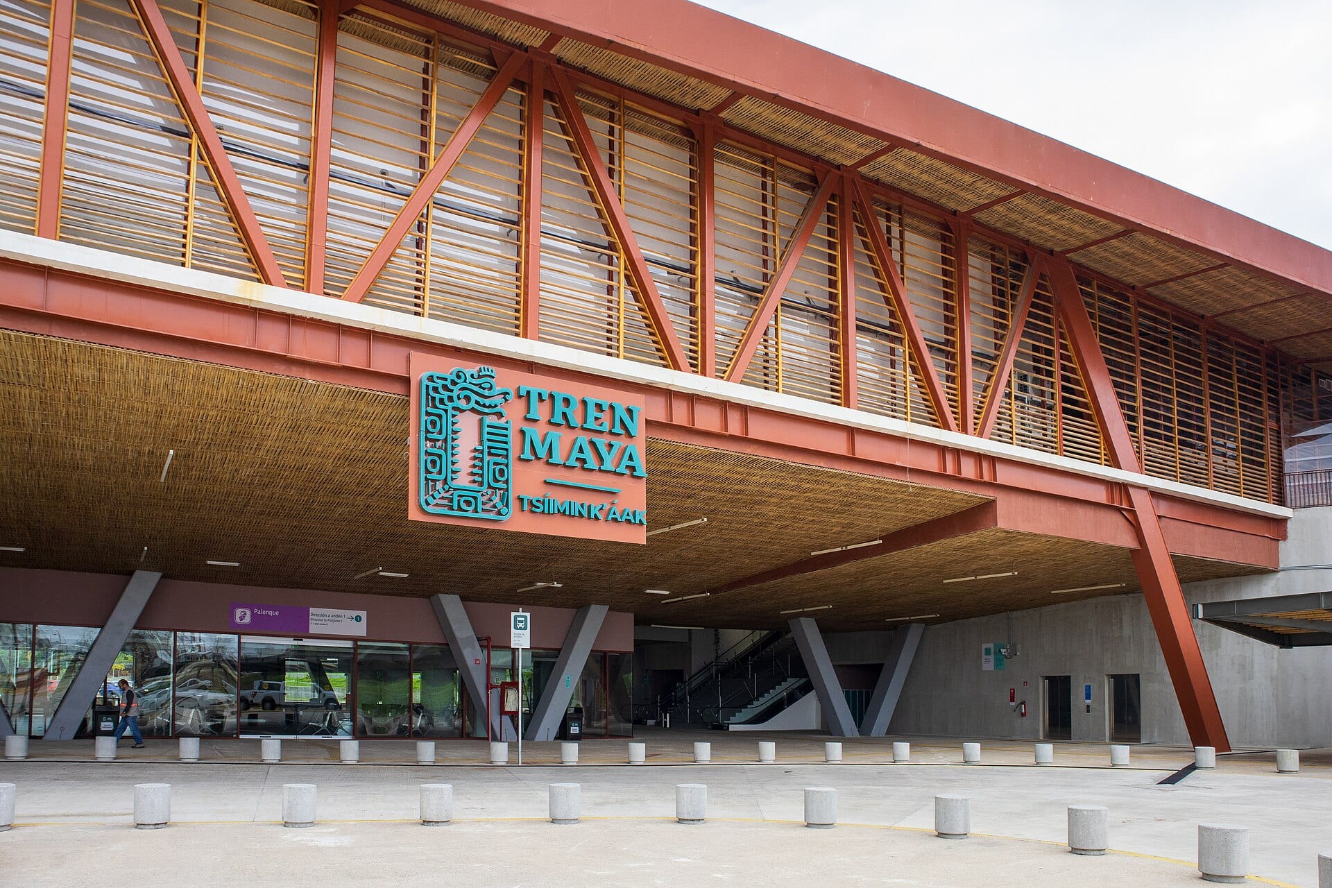 Fachada de la estación Palenque del Tren Maya, con estructura de acero rojo, techo de palma y el letrero de la empresa.