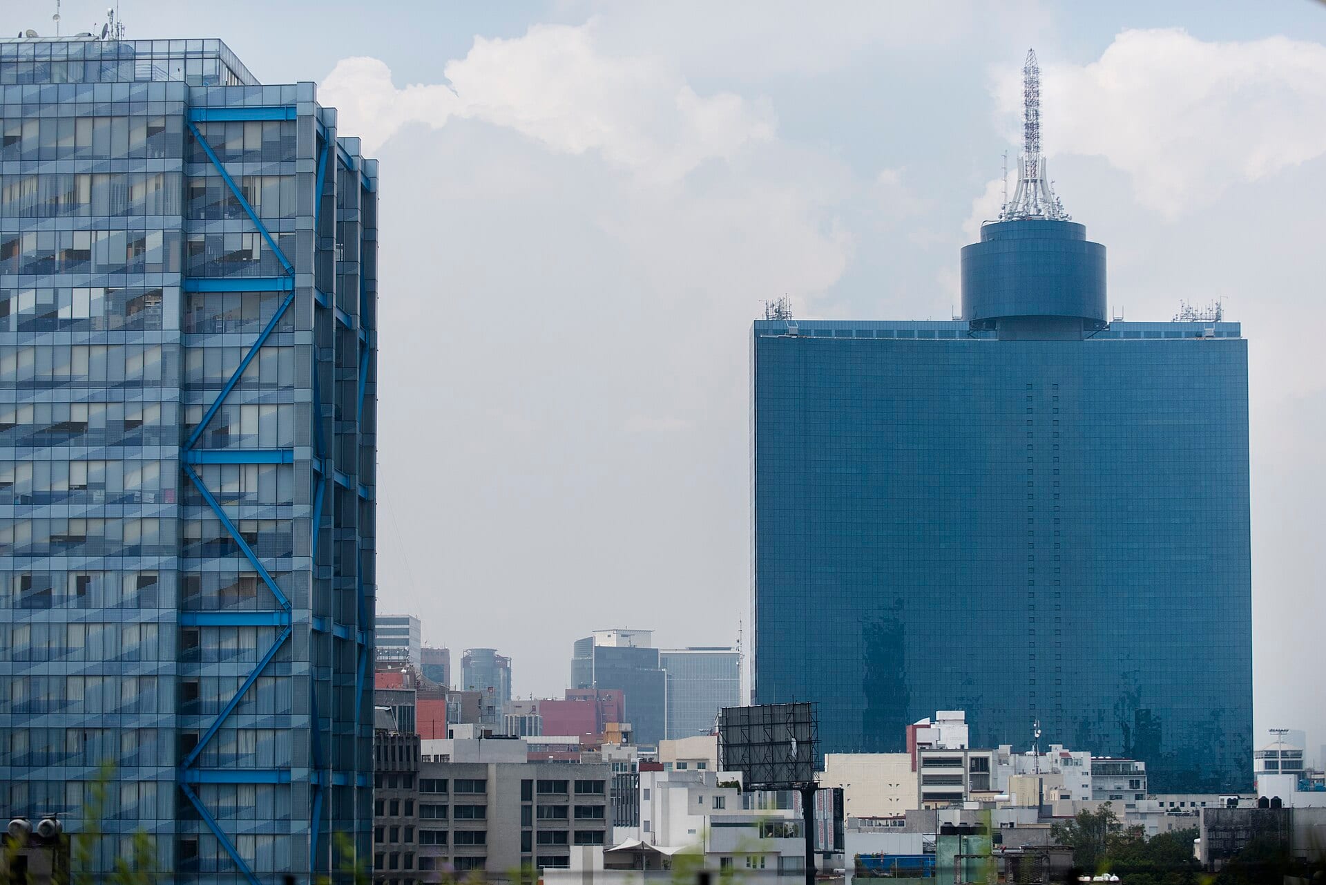 Fachada de vidrio azul del World Trade Center de la Ciudad de México, con su antena en lo alto, junto a otro edificio de oficinas.