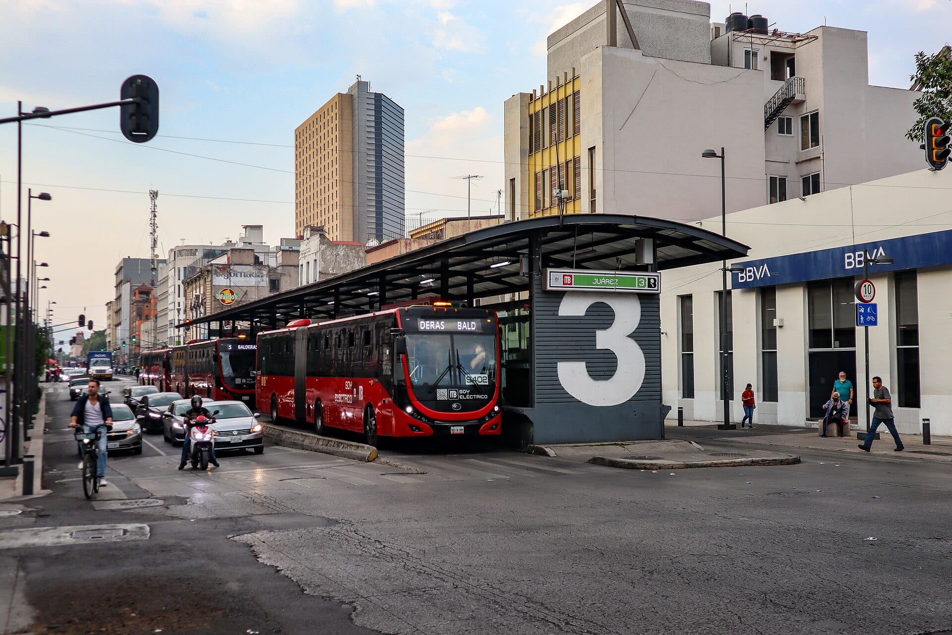 Un autobús rojo articulado entra a la estación Juárez de la Línea 3 del Metrobús, con el número 3 pintado en el módulo de acceso.