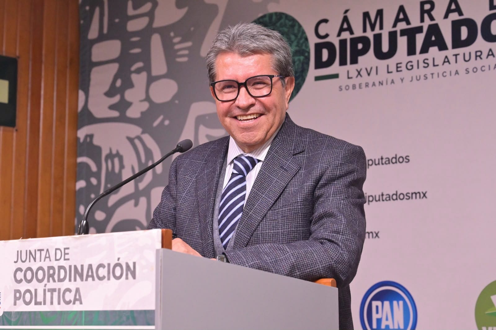Ricardo Monreal sonríe detrás del podio de la Junta de Coordinación Política, con el fondo de la Cámara de Diputados.