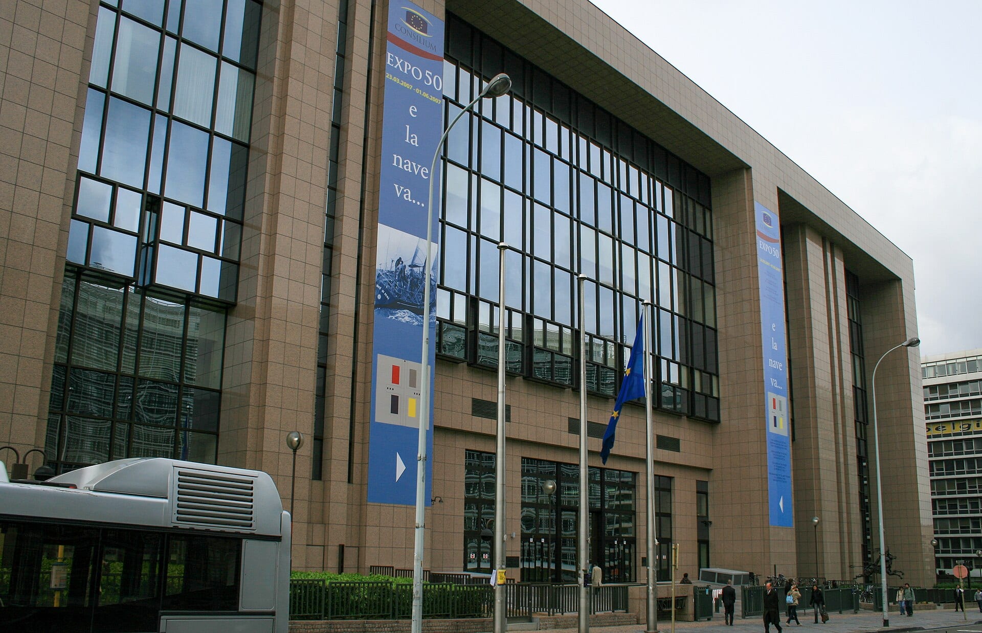 Granite and glass facade of the Justus Lipsius building, seat of the Council of the EU in Brussels, with a European flag in front of the entrance.