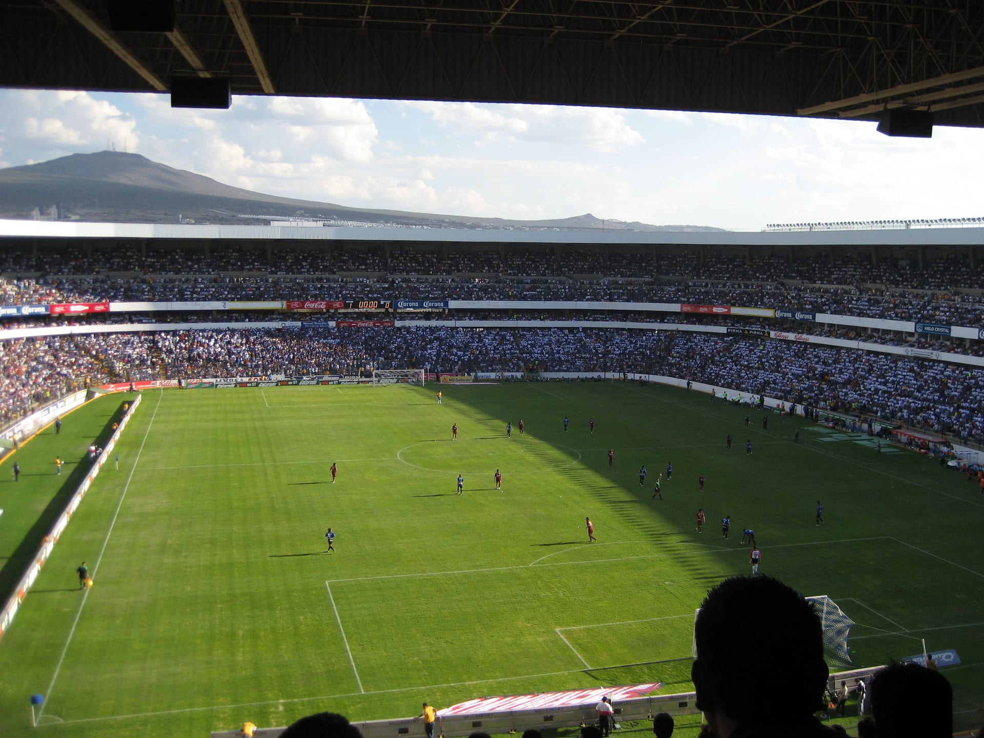 Vista desde una tribuna alta del estadio La Corregidora durante un partido de 2007, con la cancha verde, las gradas llenas y un cerro al fondo.