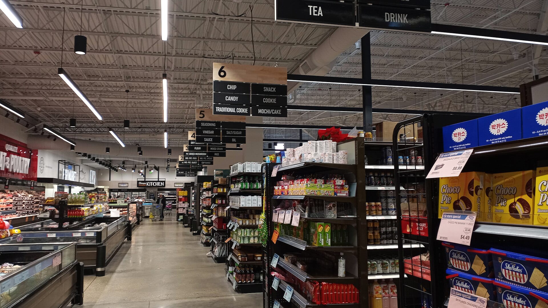 A supermarket aisle with freezer cases on the left and shelves of packaged goods on the right.