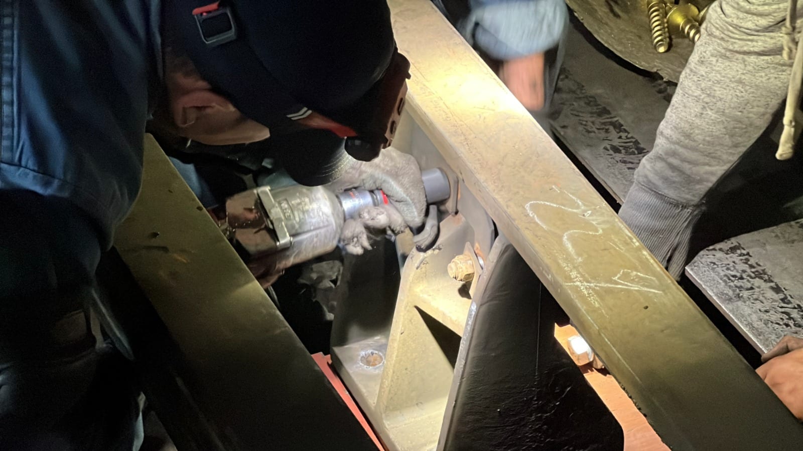 De noche, un obrero con lámpara en la frente usa una llave neumática sobre una pieza metálica de la vía, rodeado de otros trabajadores.