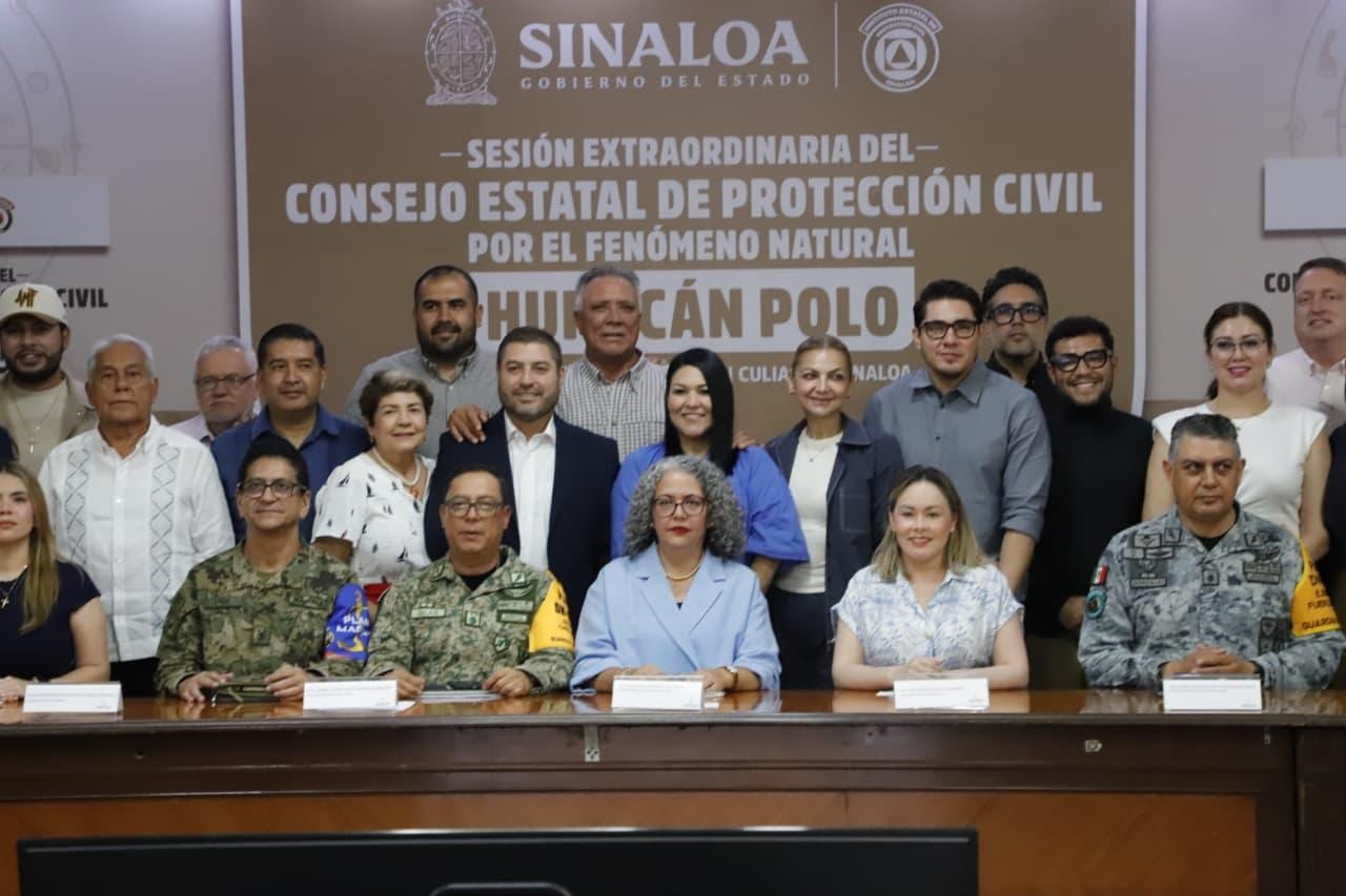Integrantes del Consejo Estatal de Protección Civil de Sinaloa posan frente a una manta que anuncia la sesión extraordinaria por el huracán Polo, en Culiacán.