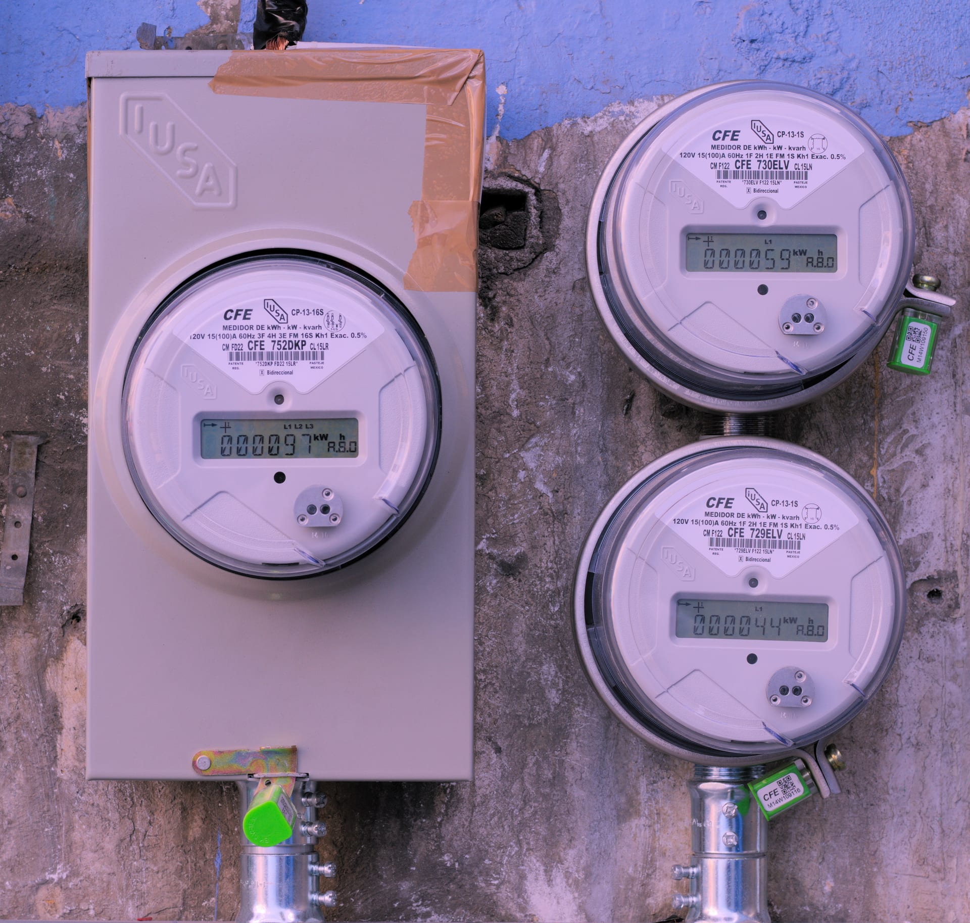 Tres medidores de electricidad de la CFE montados en una pared de concreto, con sus pantallas de kilowatts hora.