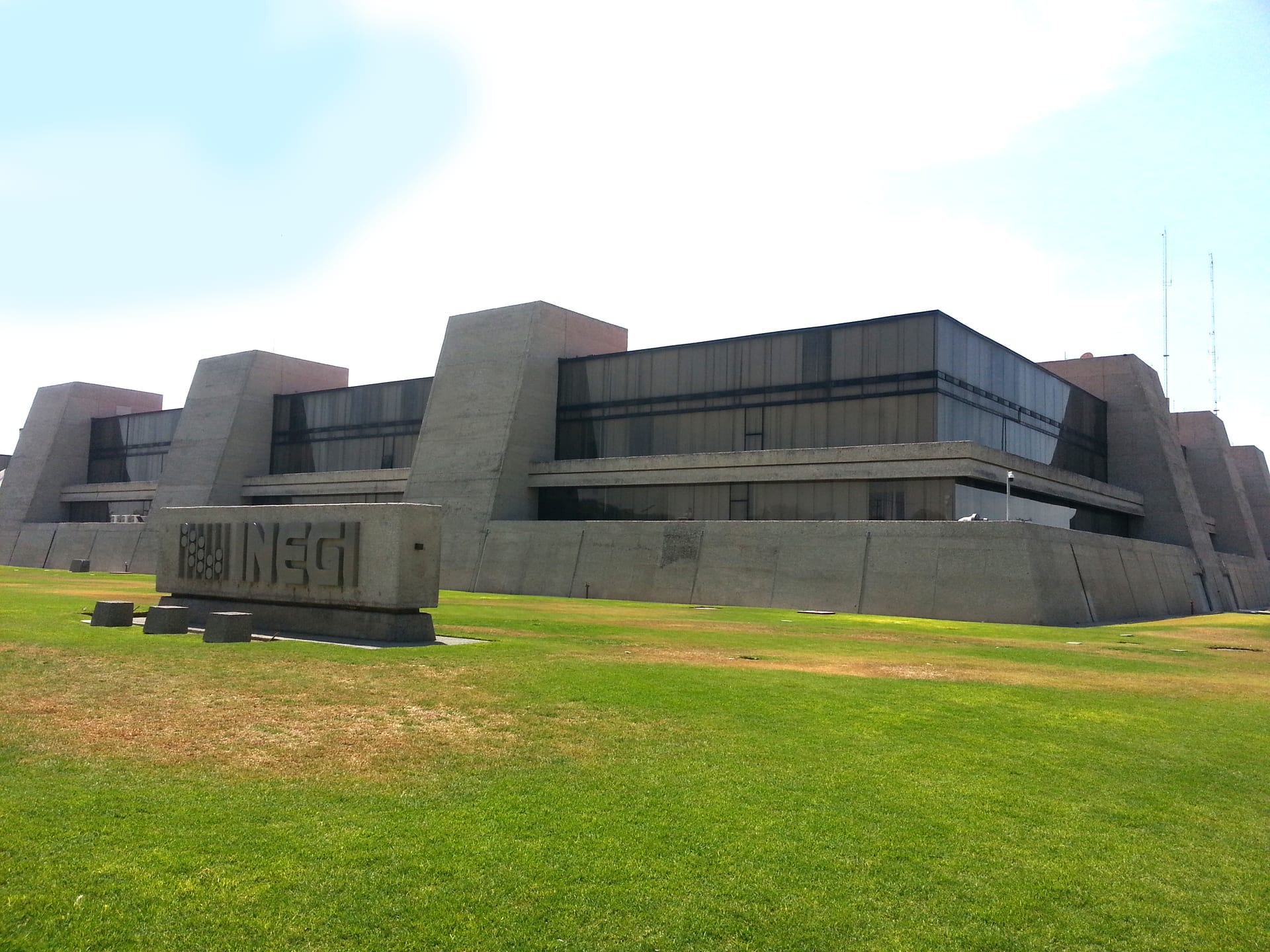 Fachada de concreto de un edificio institucional moderno, con el logotipo del INEGI grabado en una placa sobre el pasto al frente.