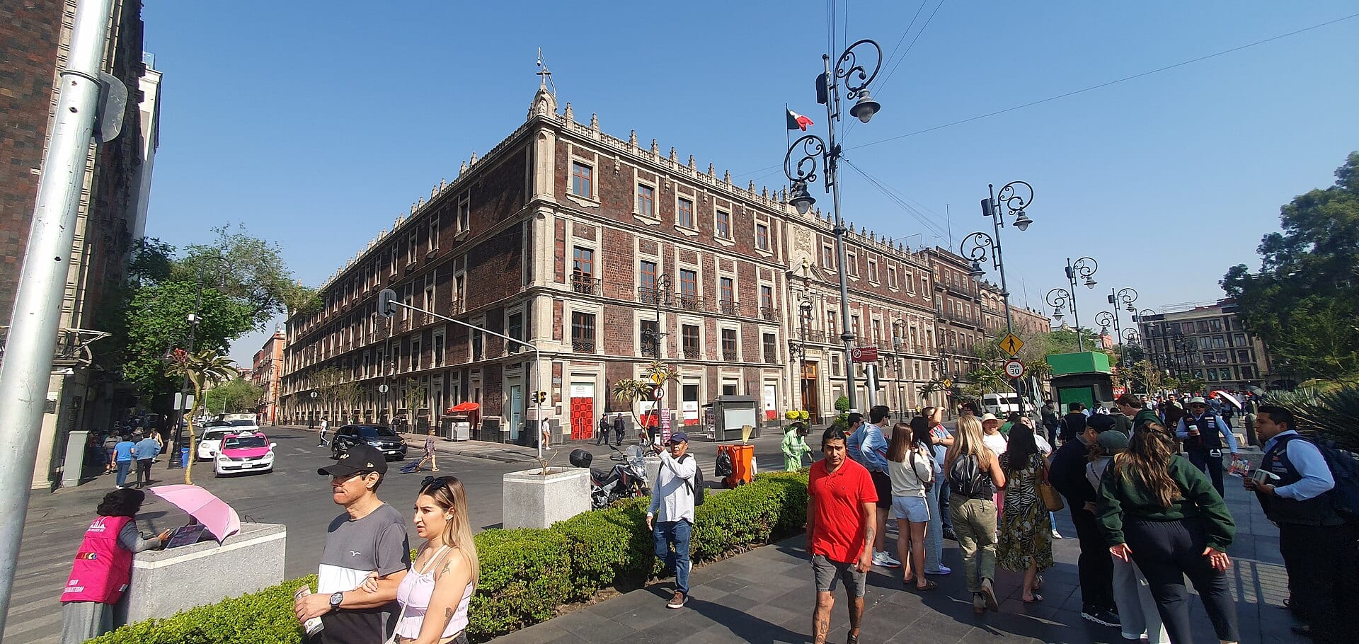 Edificio de ladrillo rojizo y cantera en una esquina del Centro Histórico, con peatones y farolas en primer plano.