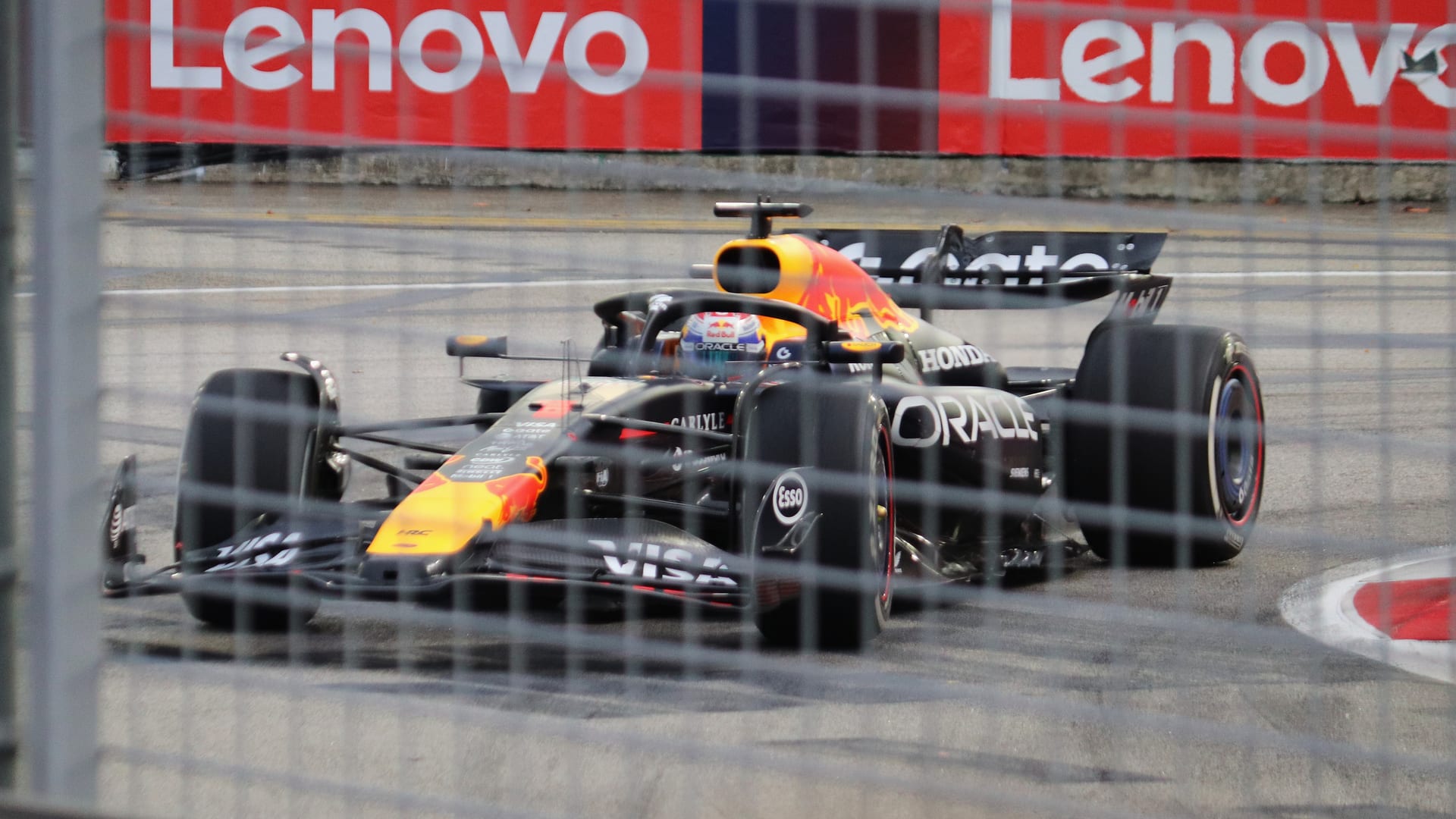 El Red Bull de Max Verstappen toma una curva del circuito de Marina Bay, visto a través de una reja, frente a publicidad roja.