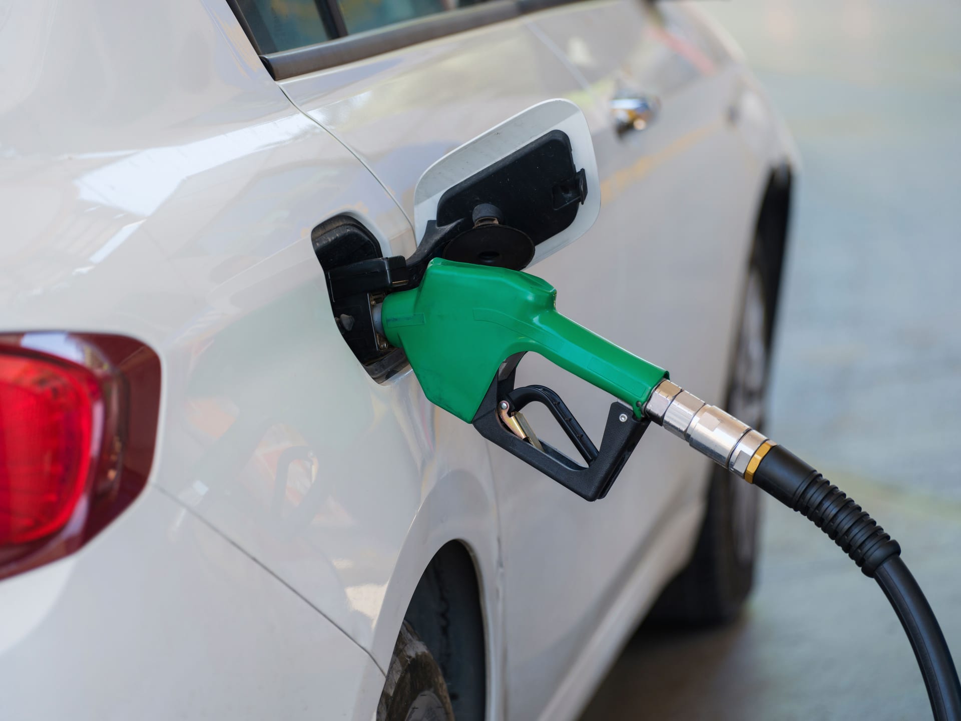 Una boquilla verde de despachador surte combustible al tanque de un auto blanco.