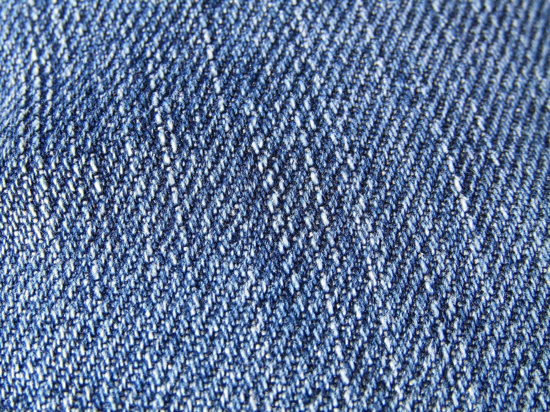 Primer plano de la trama de una tela de mezclilla azul, con hilos claros y oscuros.