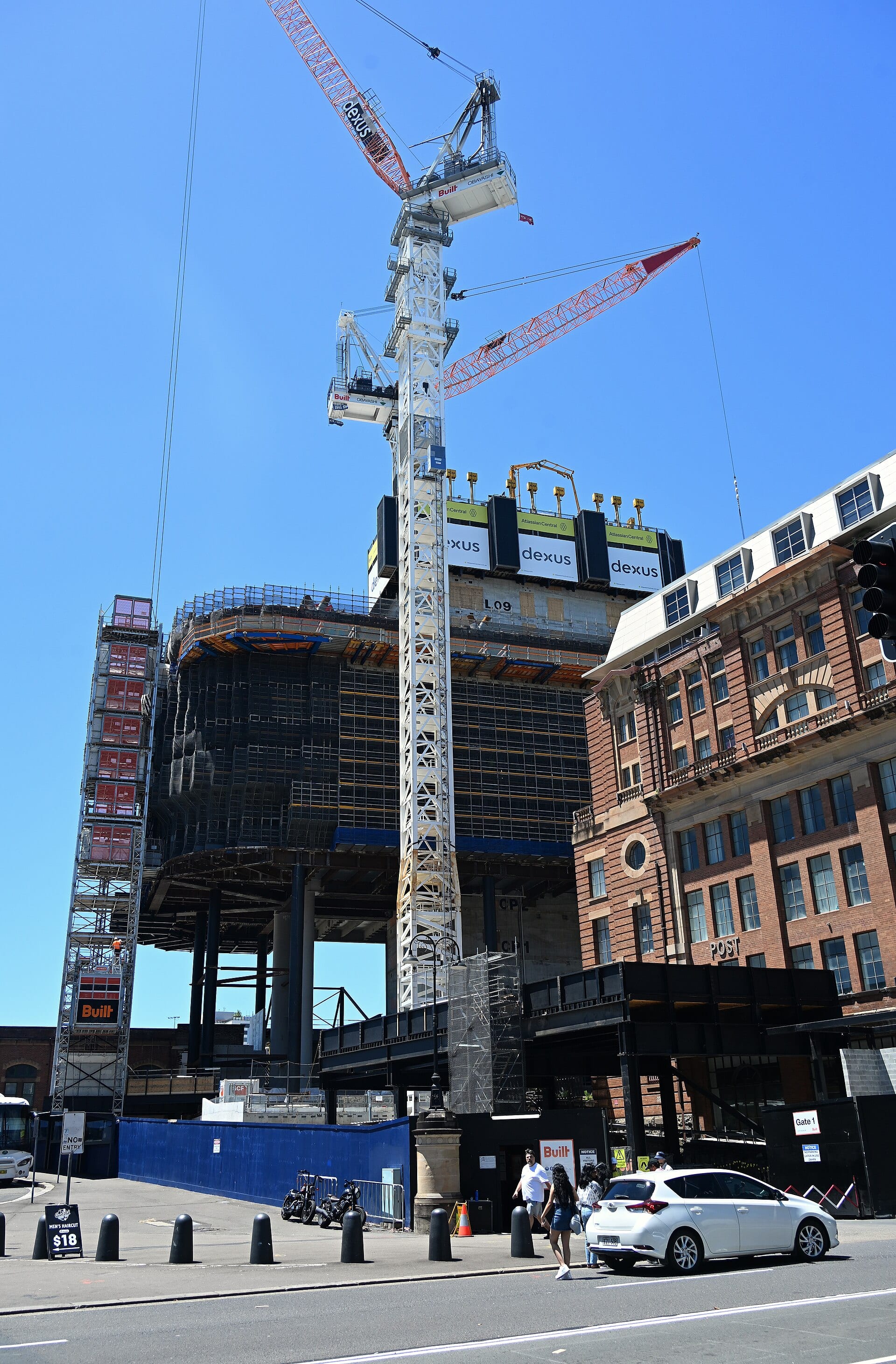 Cranes and the unfinished structure of a building with Atlassian Central signs next to a red brick building, on a Sydney street.