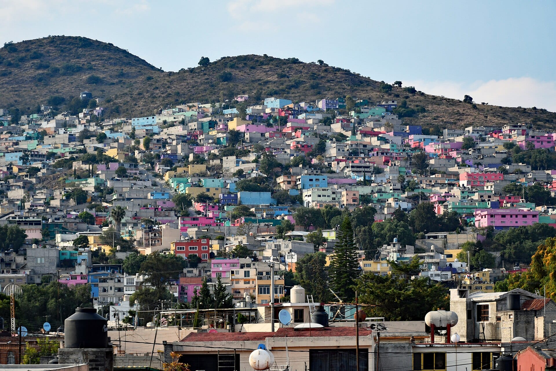 Casas de colores amontonadas en la ladera de un cerro, con tinacos en las azoteas y árboles en primer plano.
