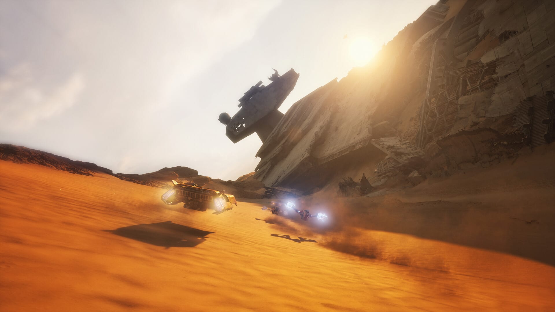 Un landspeeder dorado y una moto planeadora avanzan sobre dunas anaranjadas, junto a los restos inclinados de una nave enorme bajo un sol bajo.