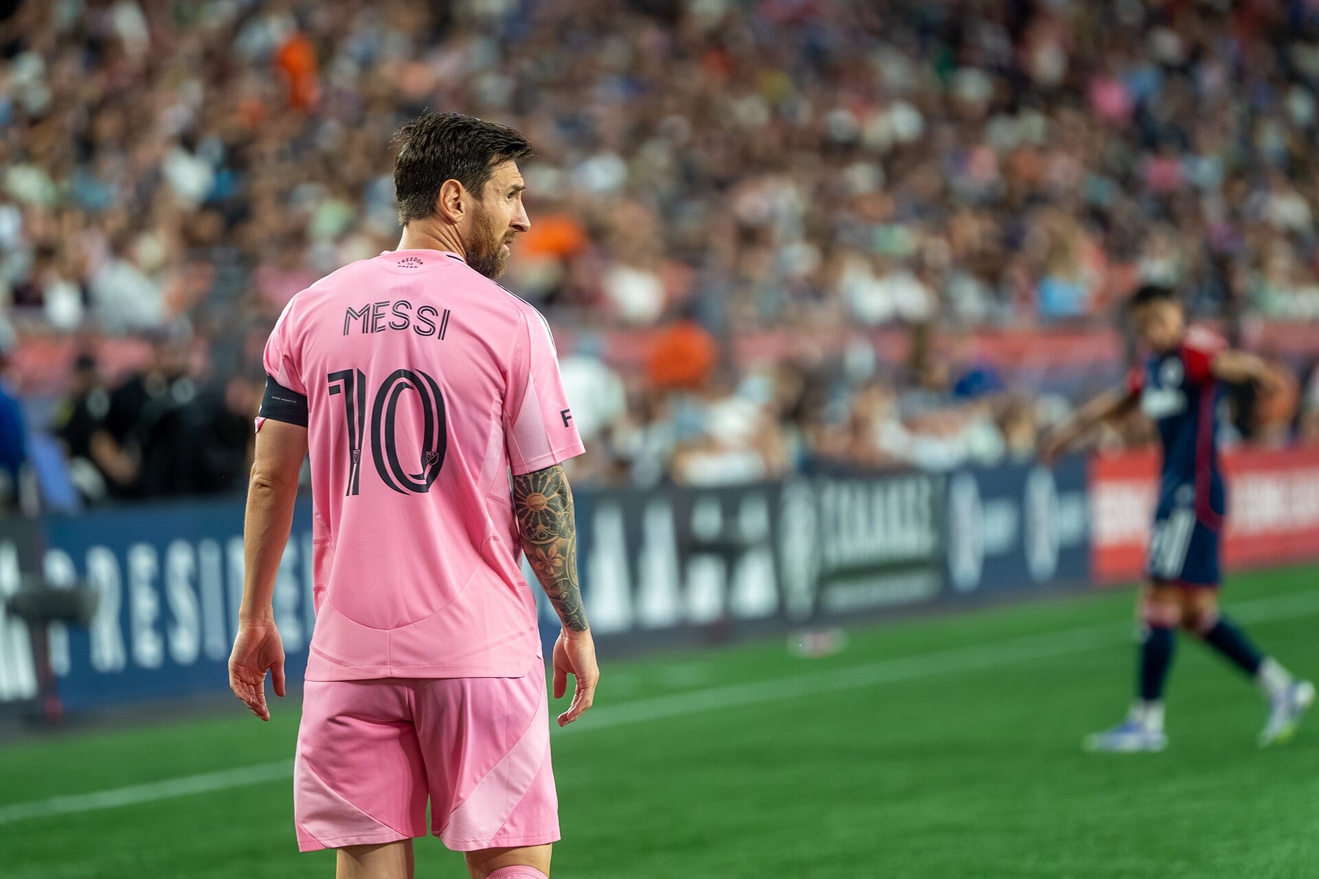 Lionel Messi, de espaldas con la camiseta rosa número 10 de Inter Miami, mira hacia la cancha con las tribunas llenas desenfocadas al fondo.
