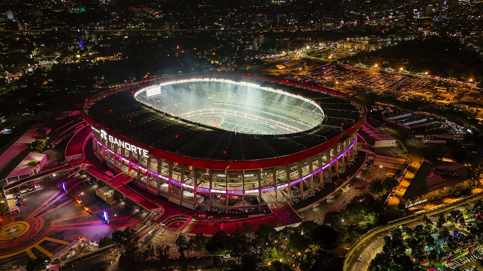 Vista aérea nocturna del Estadio Banorte, iluminado, con el letrero del estadio en la fachada.