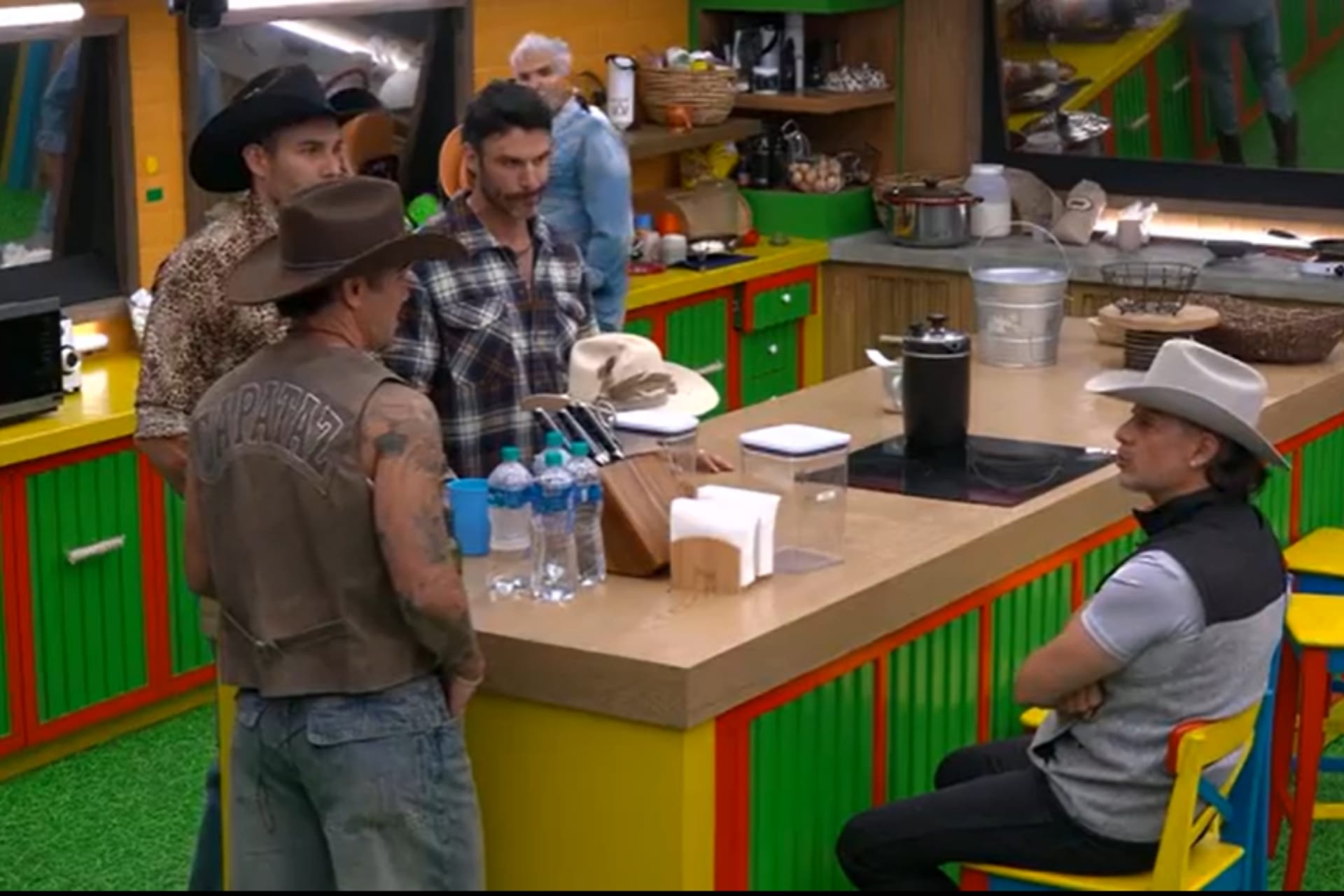 Un grupo de granjeros con sombreros vaqueros conversa de pie junto a la barra de la cocina del reality.