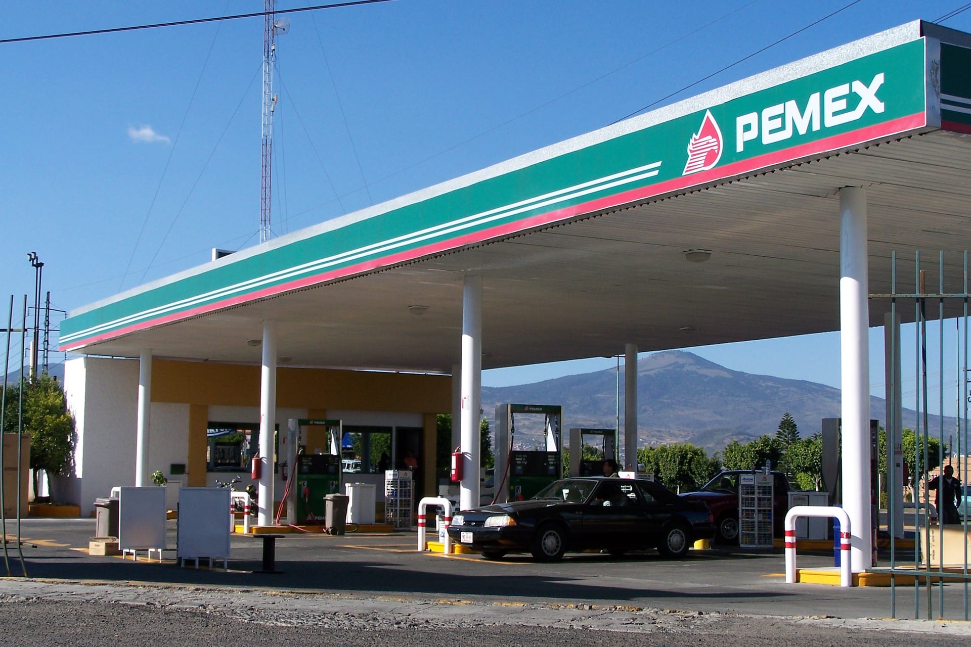Una estación de gasolina de Pemex con techumbre verde y roja y varios surtidores.