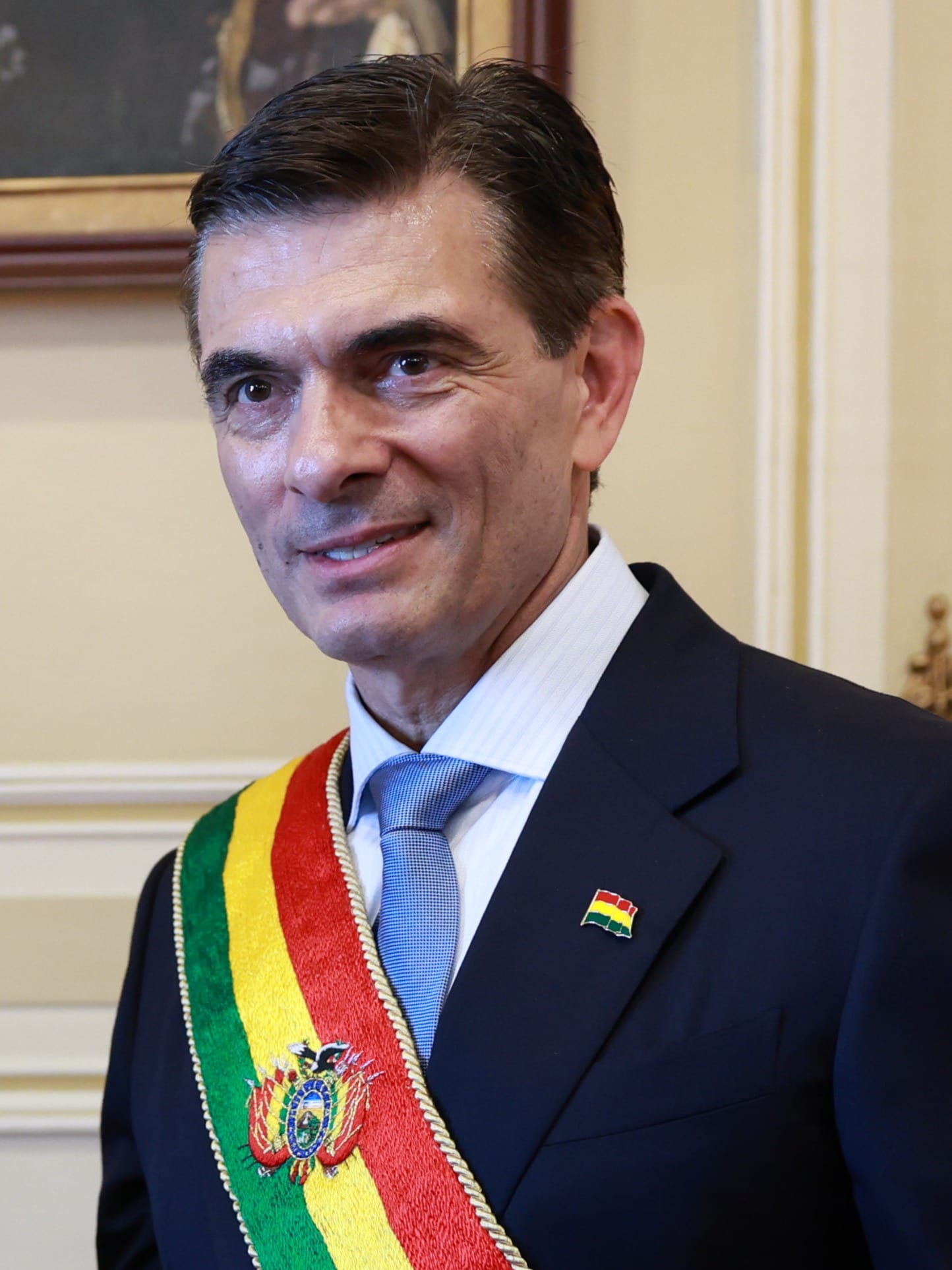 Un hombre de traje azul marino sonríe con la banda presidencial boliviana cruzada sobre el pecho.