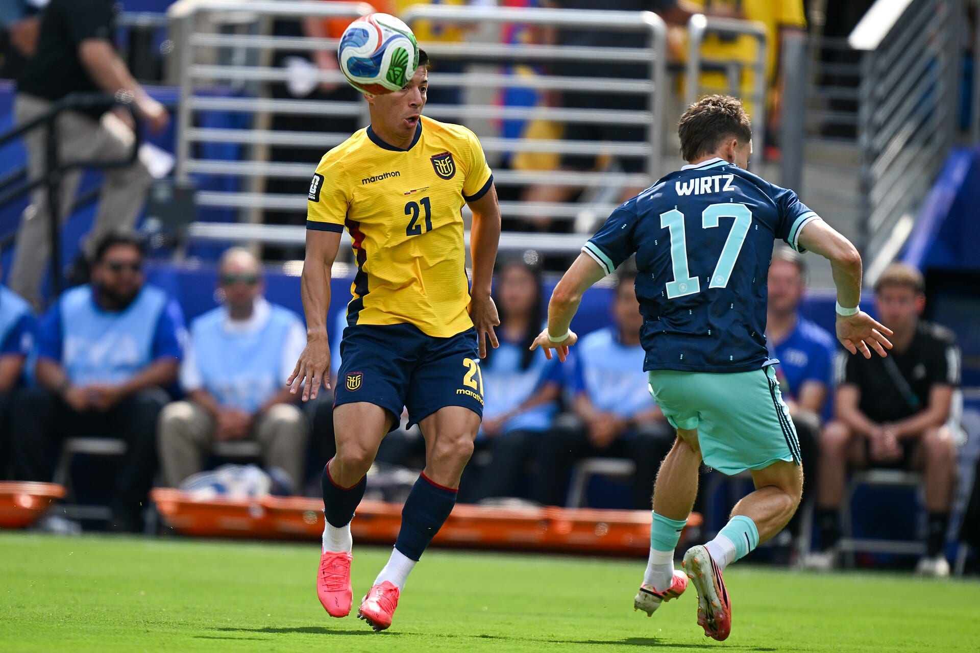 Un jugador de Ecuador con uniforme amarillo controla el balón con la cabeza mientras Florian Wirtz, con la camiseta 17 de Alemania, se acerca por la derecha.
