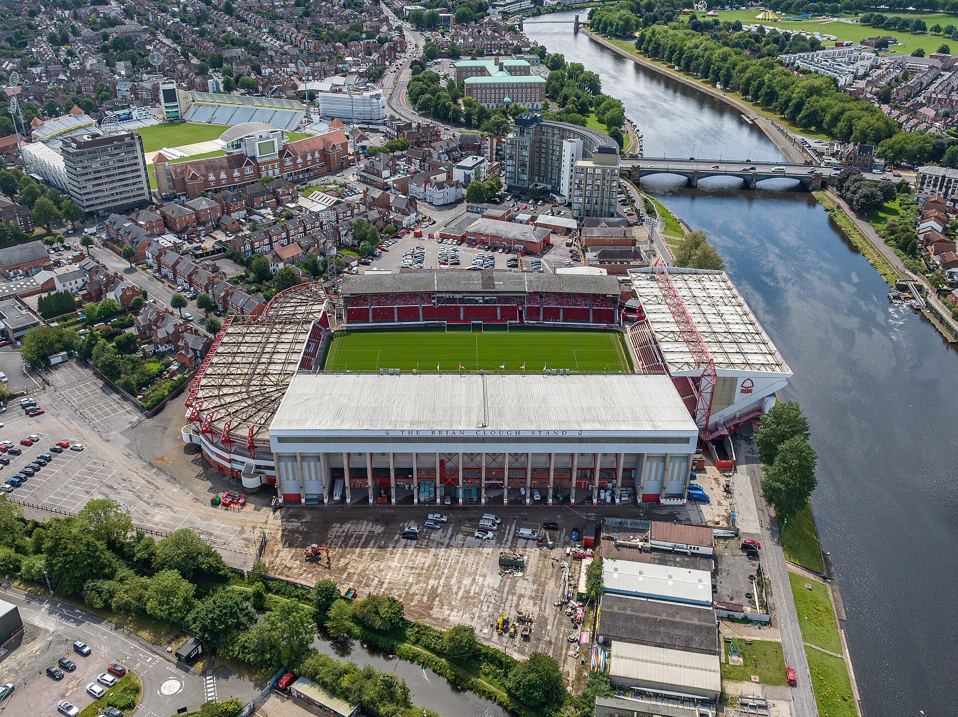 Vista aérea del City Ground de Nottingham, con la cancha verde rodeada de tribunas rojas y el río Trent a la derecha.