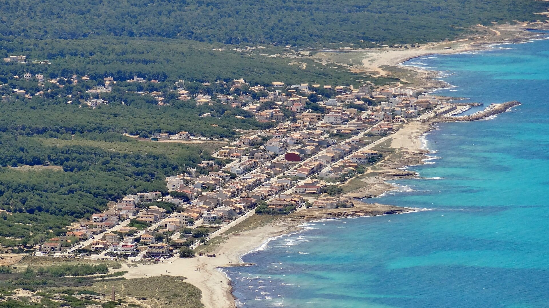 Vista aérea de casas de Son Serra de Marina entre un pinar y una costa de agua turquesa en Mallorca.