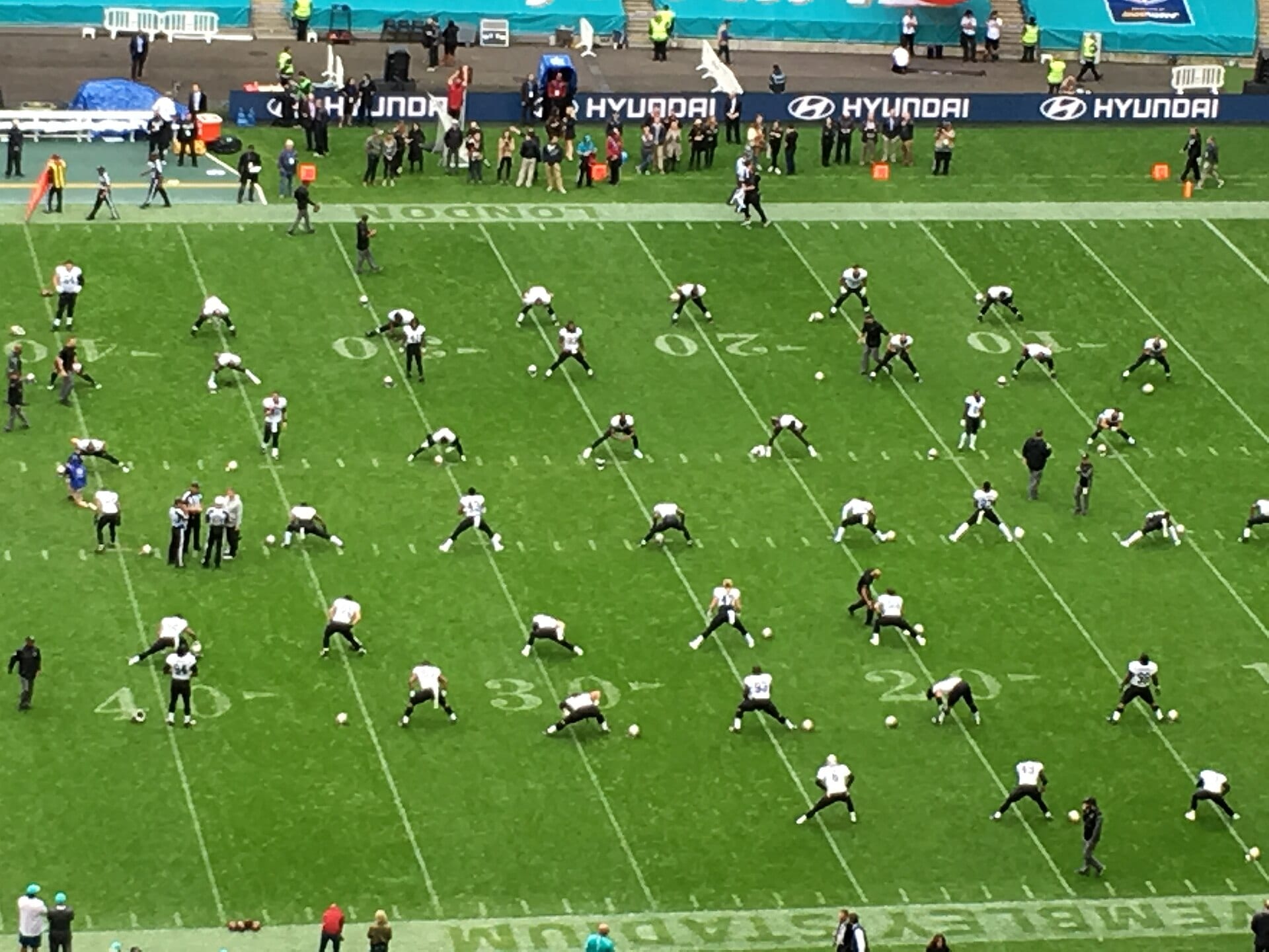 High-angle view of the Wembley turf with players in white and black uniforms stretching in rows during a warm-up.