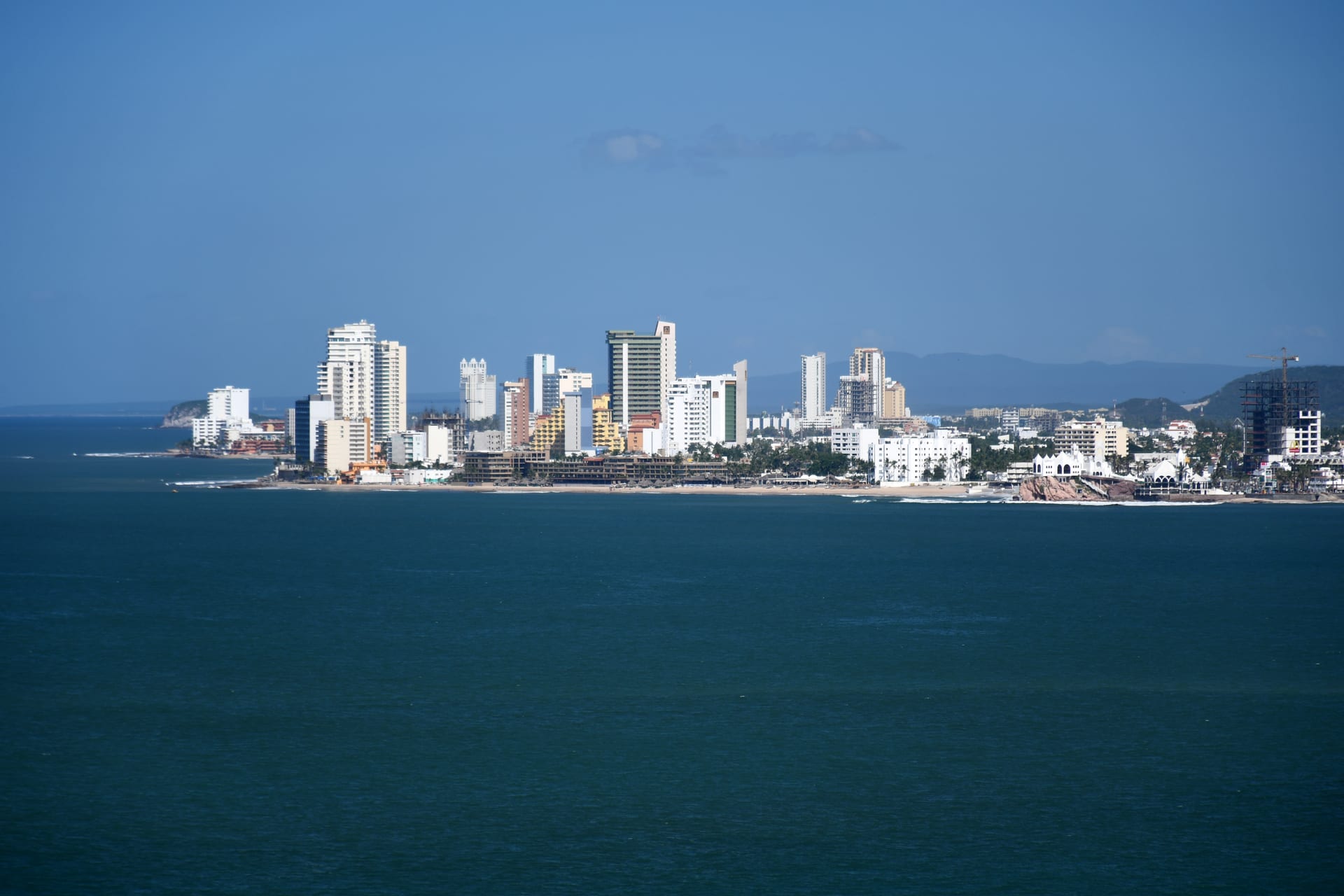 Edificios de la Zona Dorada de Mazatlán junto a la costa, vistos desde el mar con el cielo despejado.
