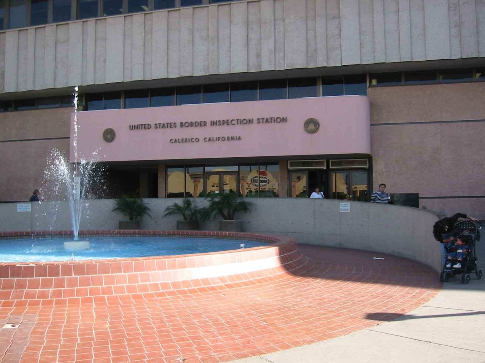 Fachada rosada del edificio de inspección fronteriza de Estados Unidos en Calexico, con una fuente en primer plano.