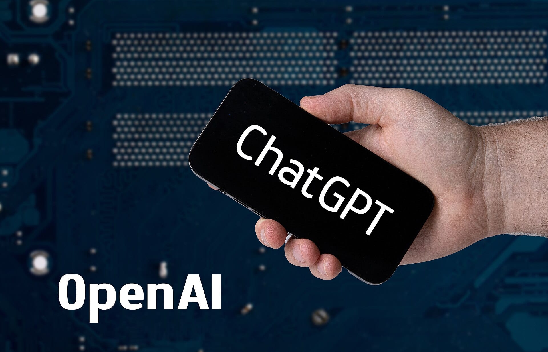 A hand holds a smartphone showing the word ChatGPT on its screen, against a blue circuit-board background with the name OpenAI.