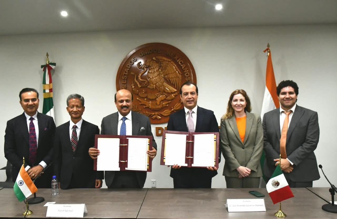 Mexican and Indian delegations hold folders with the signed Terms of Reference at a table with flags.