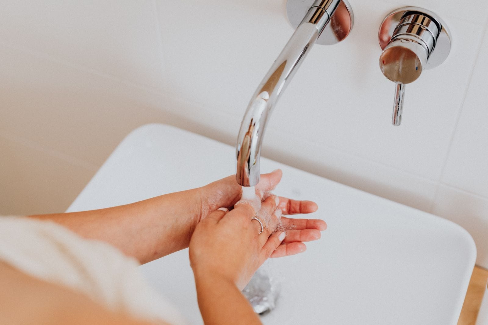 Primer plano de unas manos bajo el chorro de agua de una llave moderna, sobre un lavabo de baño.