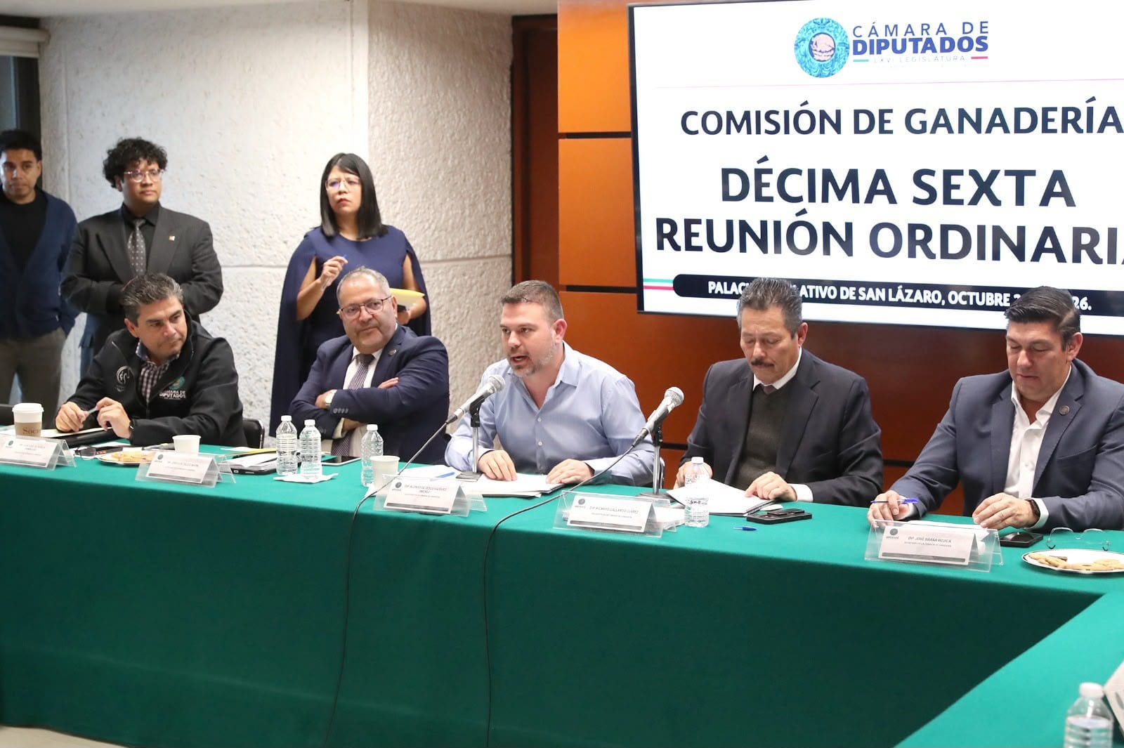 Cinco diputados sentados tras una mesa con mantel verde; uno habla al micrófono. Detrás, una pantalla dice "Comisión de Ganadería, Décima Sexta Reunión Ordinaria".