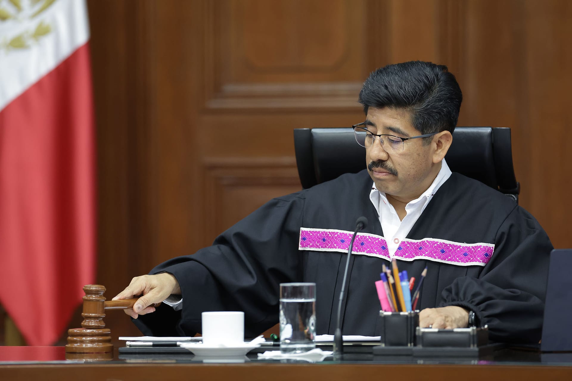 Un ministro de la Suprema Corte, con toga negra bordada, golpea con un mazo el estrado de la sala; a su izquierda se ve una bandera de México.