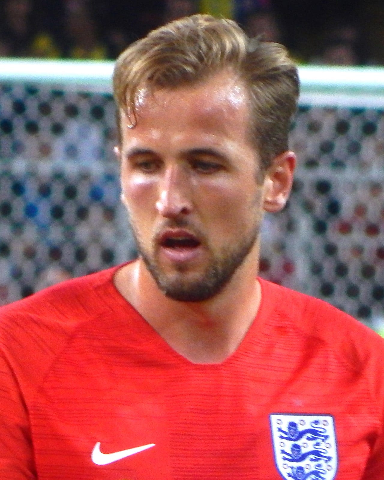 Primer plano de Harry Kane con la camiseta roja de Inglaterra, la mirada baja y una portería detrás.