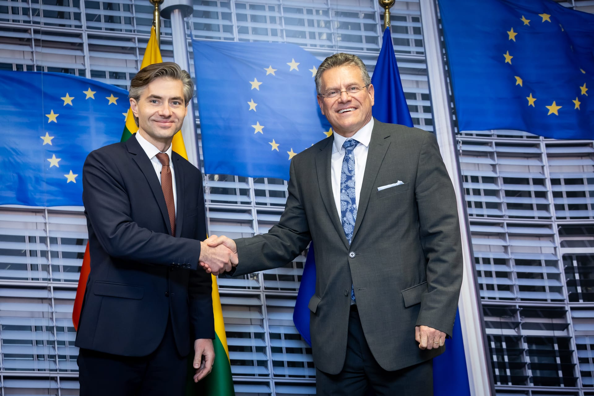 Maroš Šefčovič, comisario europeo de Comercio, sonríe y da la mano a un funcionario lituano frente a banderas de la Unión Europea, en una foto de diciembre de 2024.