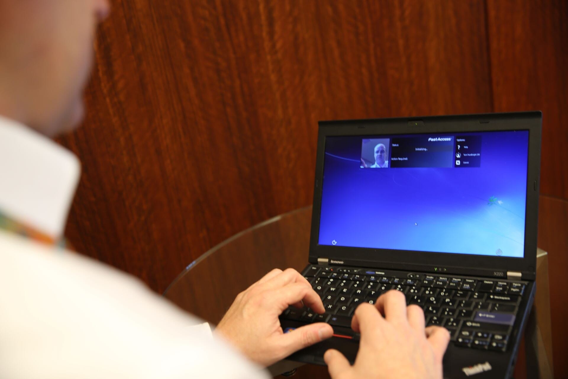 Un hombre teclea en una laptop cuya pantalla muestra una pequeña imagen de su rostro y un panel de reconocimiento facial.