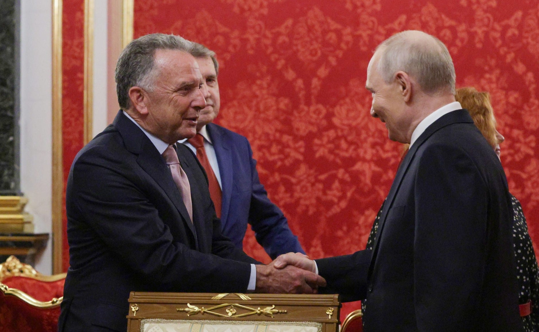 El presidente ruso Vladímir Putin estrecha la mano de Steve Witkoff en un salón de paredes rojas, con un asesor detrás.