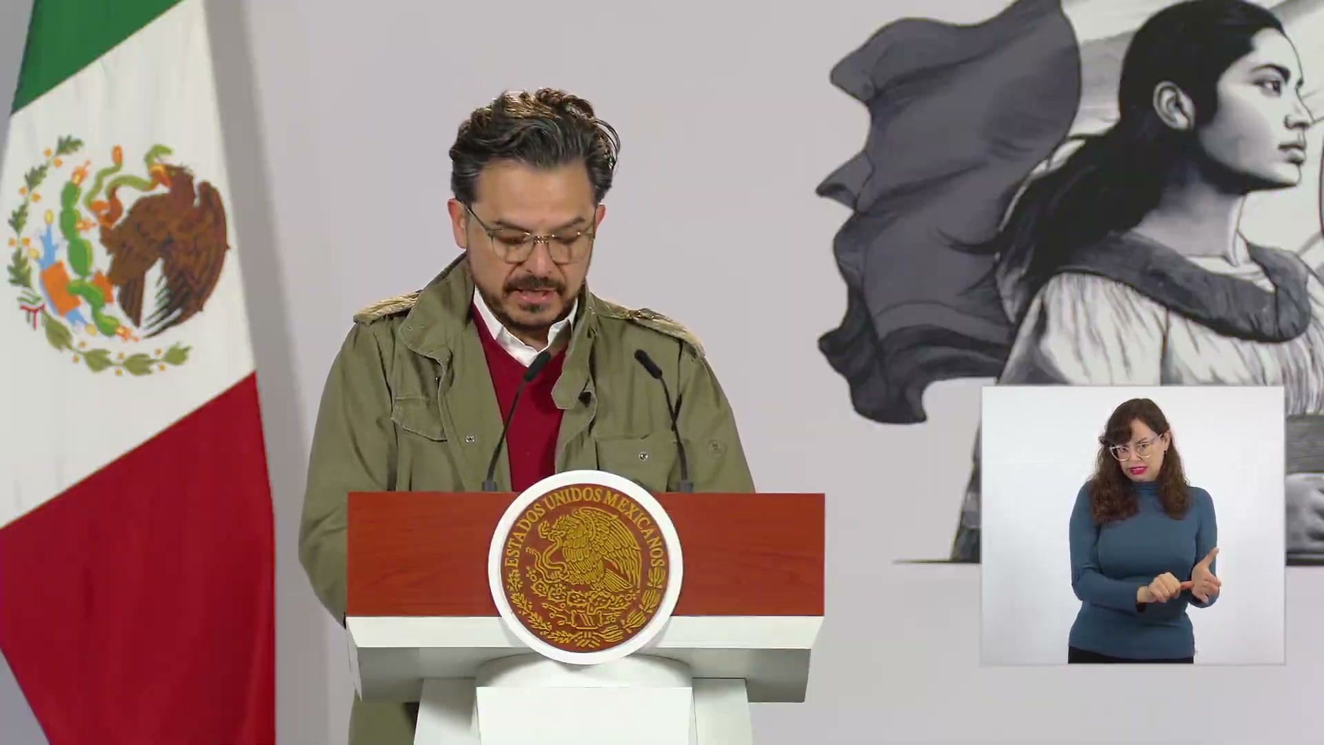 Zoé Robledo, de chamarra verde olivo, habla desde el podio de la conferencia matutina; a su derecha, una intérprete de lengua de señas.