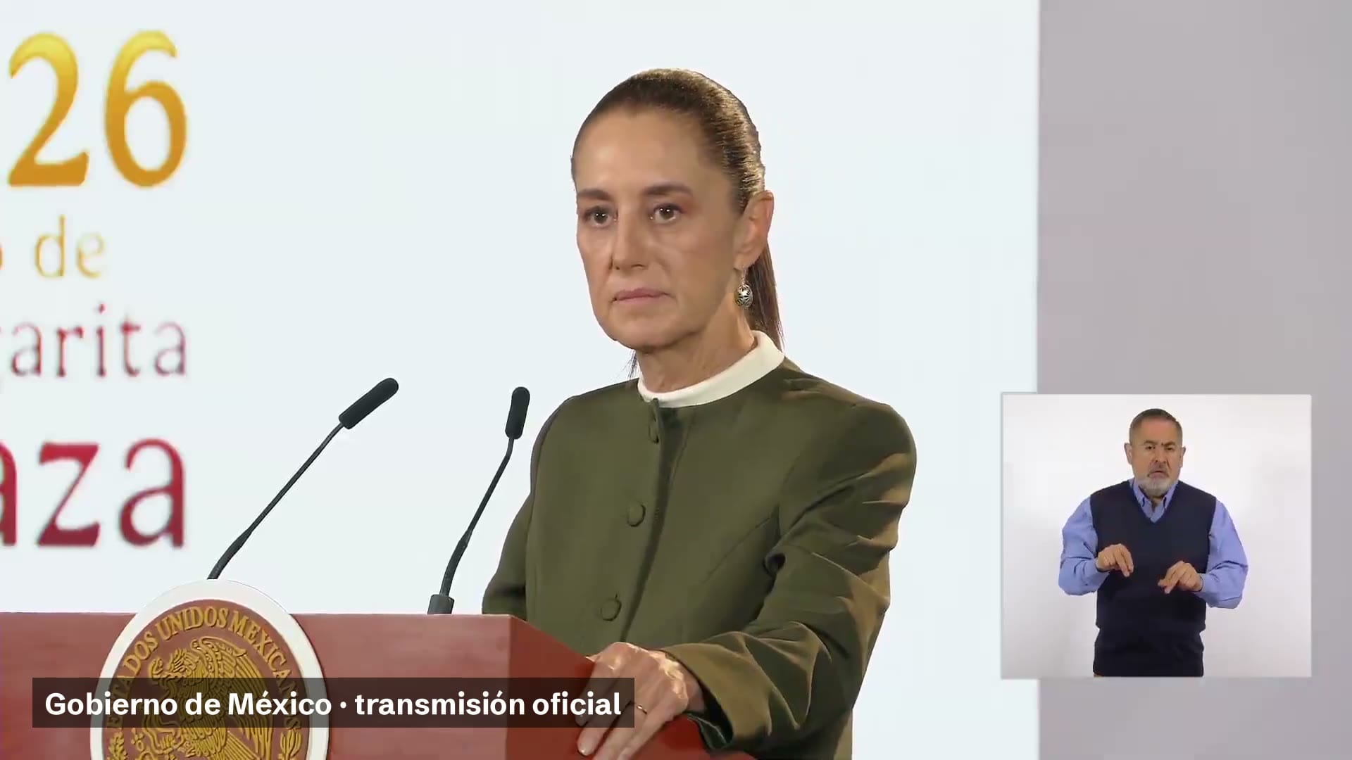 La presidenta Claudia Sheinbaum, de pie ante el atril con el escudo nacional, y a la derecha un intérprete de lengua de señas.